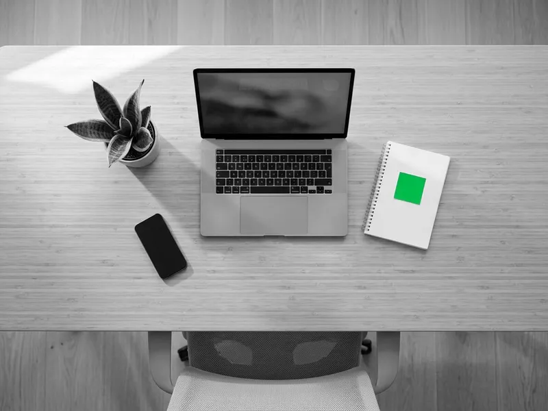 A tidy desk with a laptop, phone and notebook, seen from above